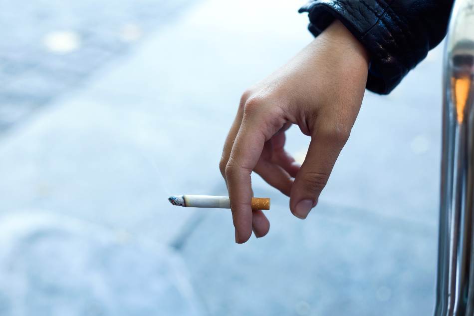 mão masculina segurando o cigarro entre o indicador e dedo do meio