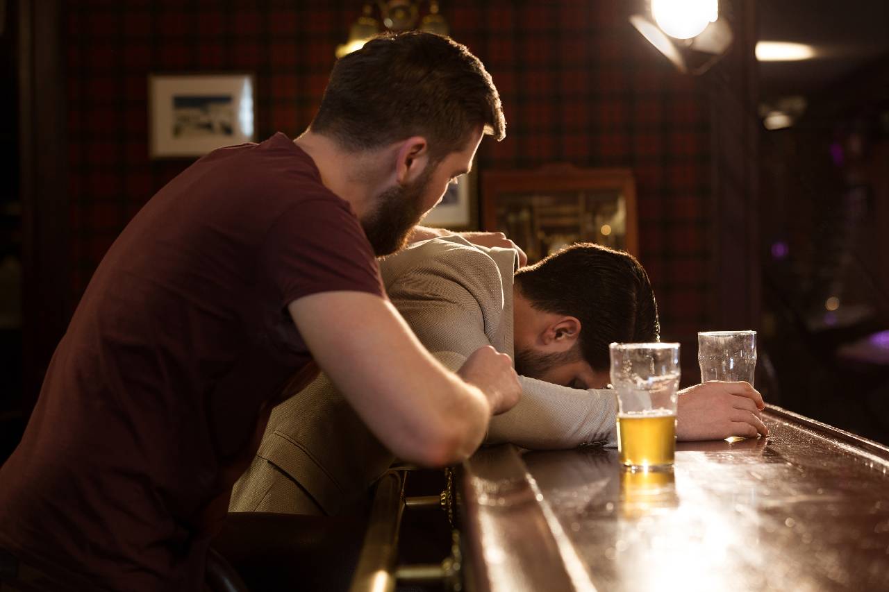 homem ajudando amigo bebado em bar